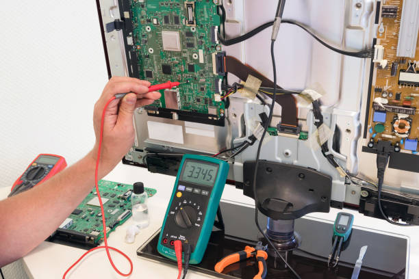 The consumer electronics repair engineer measures the voltage on the television board